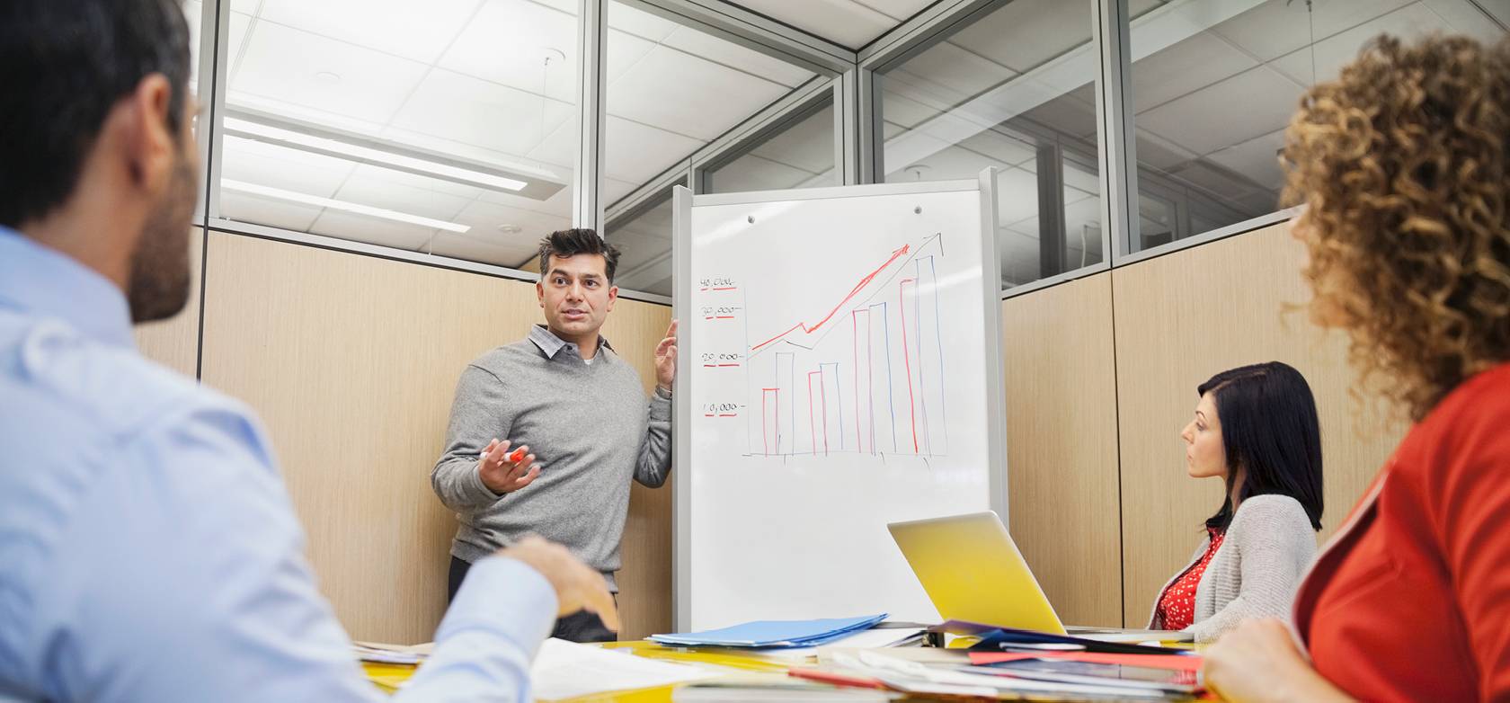 Man explaining with a graph drawn on a whiteboard in a small meeting room
