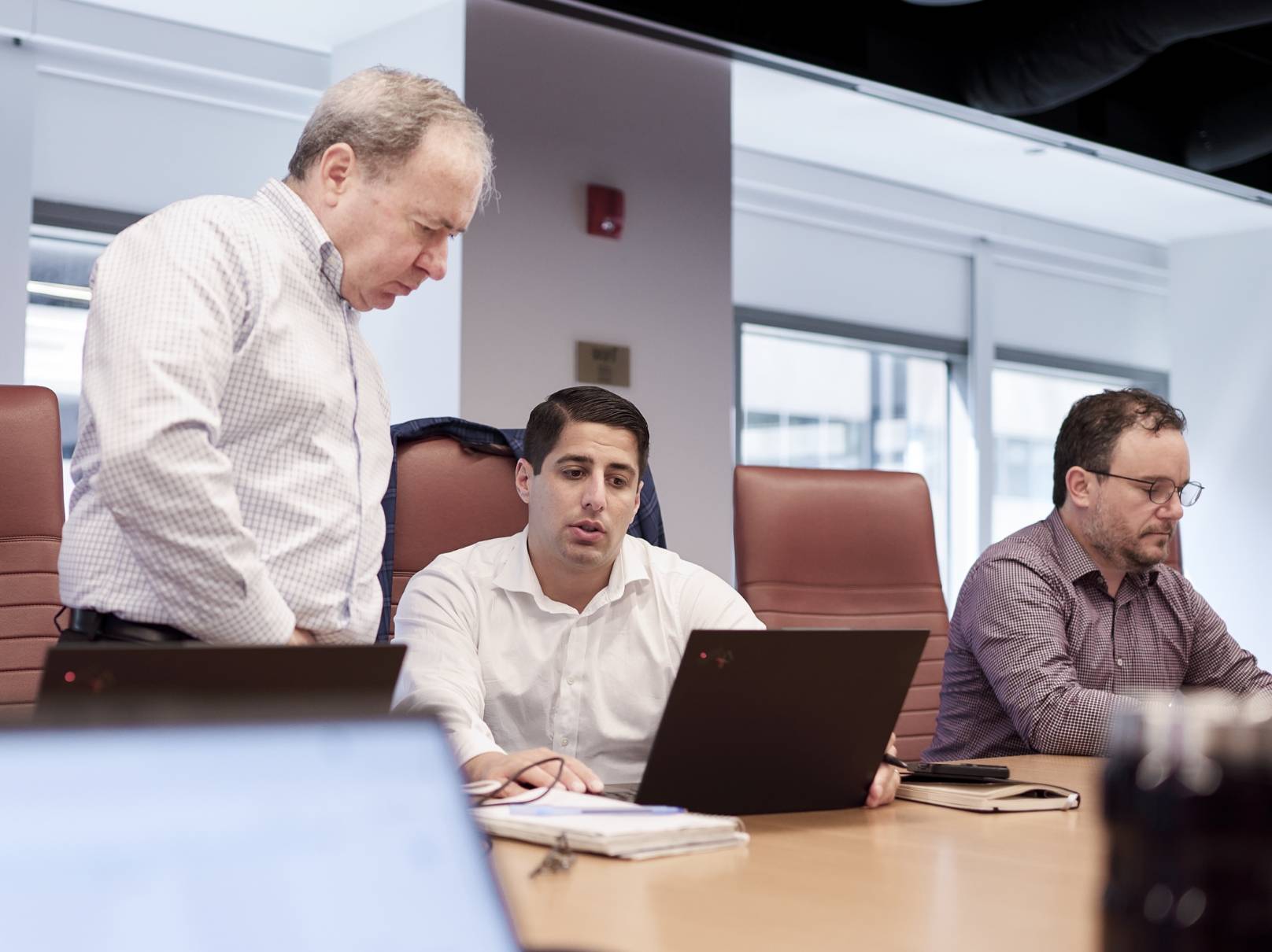 Three Novo Advisors team members at a conference room table, two of them are looking at a laptop together.