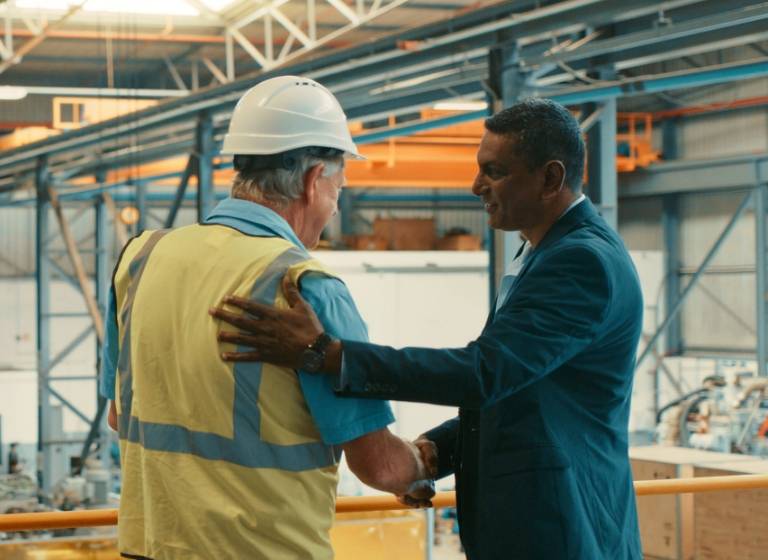Close up shot of business man patting the back of a old factory worker